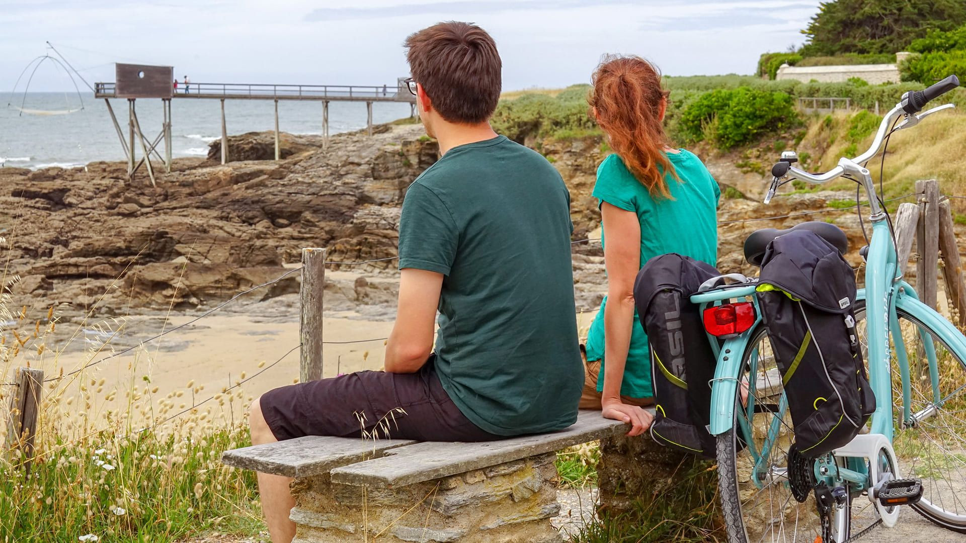 Cyclistes sur un banc face à la mer et à un carrelet - Côte de Jade - France