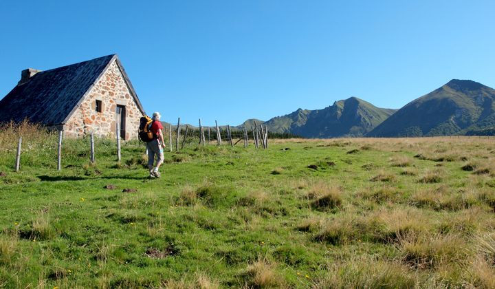 Randonneur passant devant un buron en pierre - Auvergne - Massif central