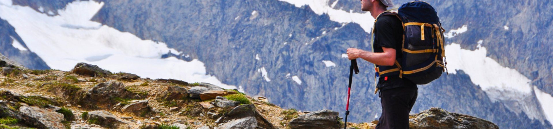 Randonneur avec sac à dos et bâtons face aux sommets enneigés - Alpes