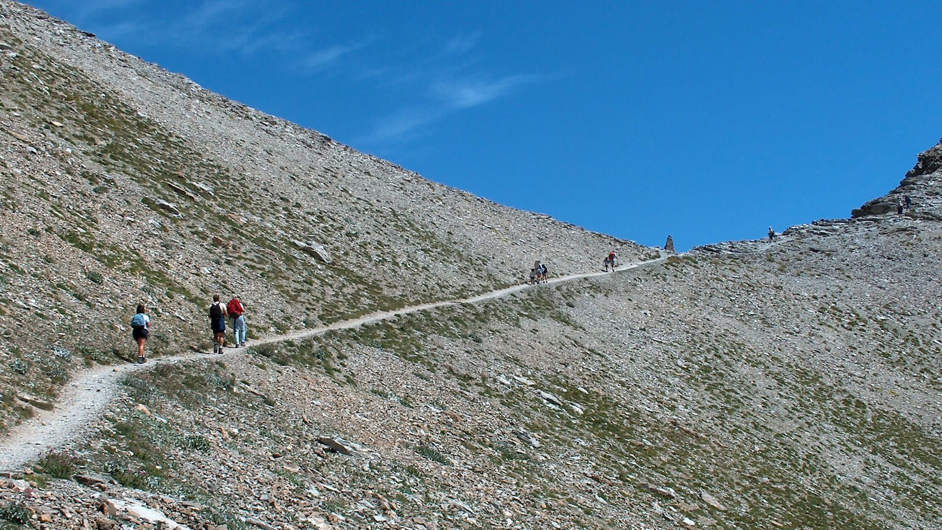 Randonneurs montant vers un col par un sentier d'éboulis - Alpes - France