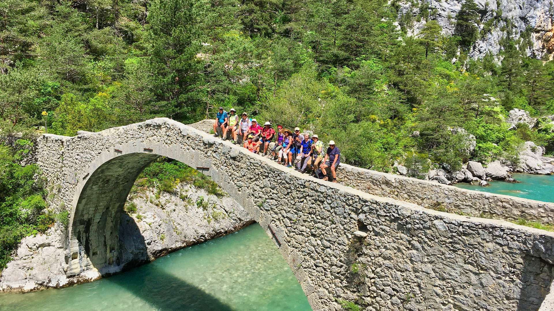 Randonneurs sur un pont de pierre au-dessus d'une rivière turquoise
