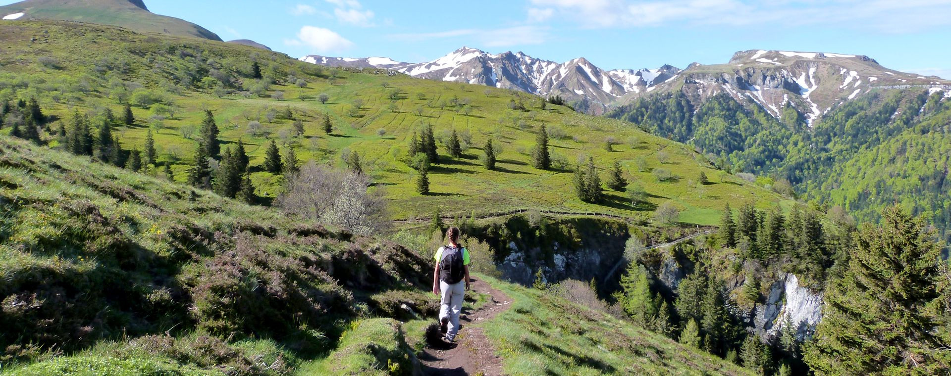 Randonneur sur un sentier face aux monts enneigés - Auvergne - Massif central