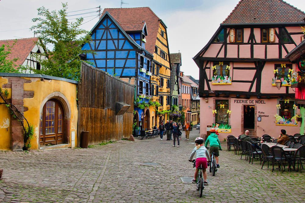 Cyclistes dans une rue pavée aux maisons à colombages - Alsace - France