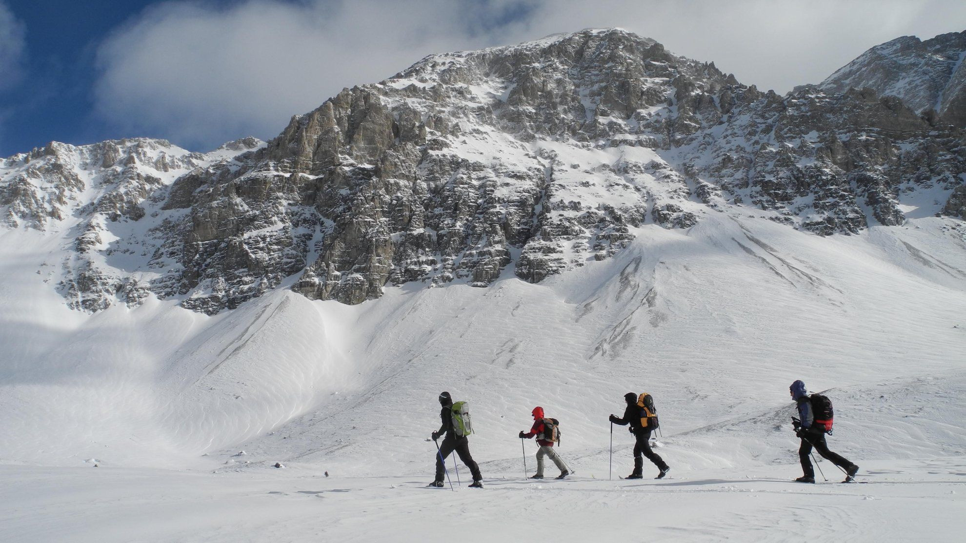 Groupe en raquettes traversant un névé sous un sommet rocheux - Alpes - France