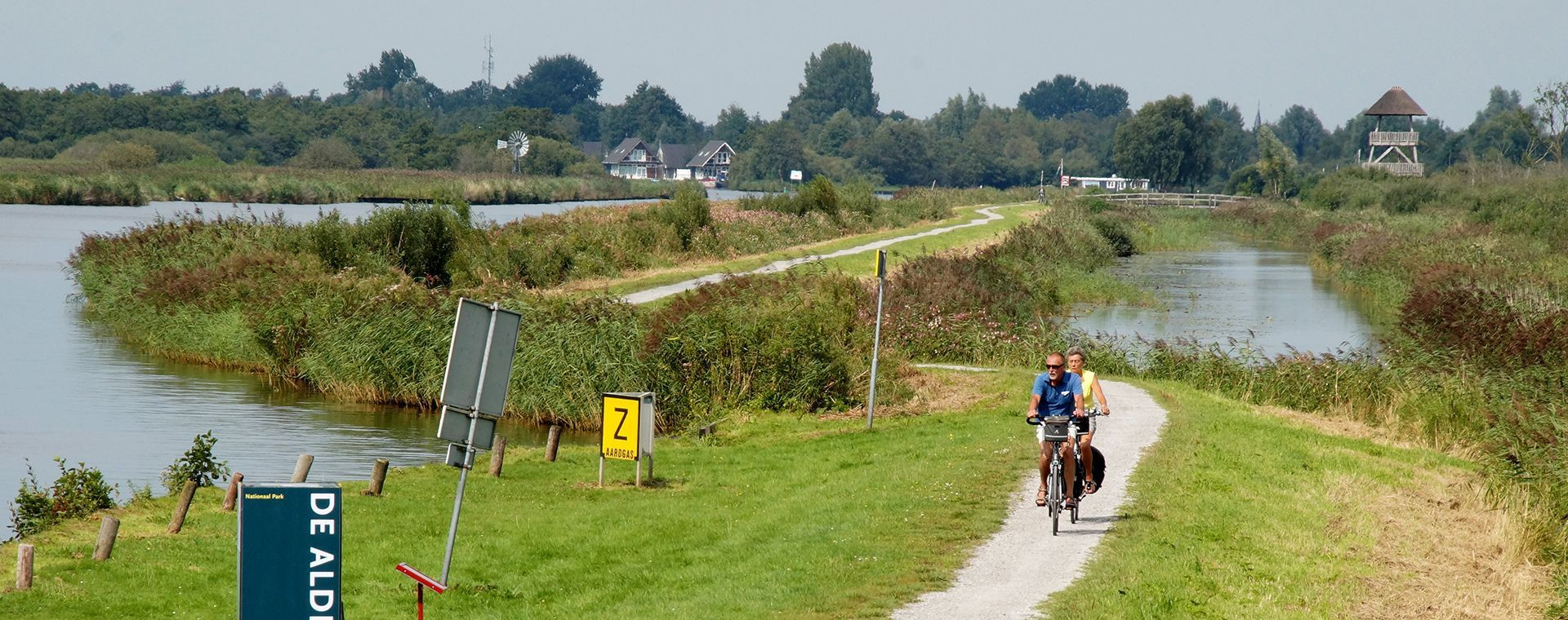 Cyclotouristes sur une digue entre les canaux - Frise - Pays-Bas